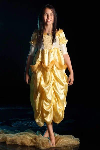 12岁的少女穿着黄色丝质连衣裙 赤脚站在一片漆黑的水域里 身材苗条 美丽而快乐 黑发少女 倾盆大雨中的感情 — 图库照片