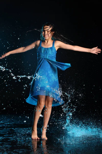 在一个黑色的水族馆里 12岁的女孩穿着蓝色的连衣裙 光着脚 身材苗条而又顽皮 一头黑发 倾盆大雨中的感情 图库照片