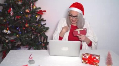 Noel aile içi tebrikleri. Evde gülümseyen kız bilgisayarını kullanarak Noel Baba şapkalı arkadaşları ve aileleri arıyor. Kameraya bakan ve el sallayan bir kadın. 4k video