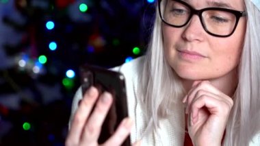 Noel aile içi tebrikleri. Evde gülümseyen kız, Noel Baba şapkalı aile ve arkadaşları için cep telefonu kullanıyor. Kameraya bakan ve el sallayan bir kadın. 4k video