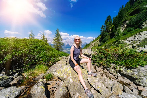 Güzel bir yaz günü Alp dağlarında yürüyüş yapan bir kadın Avusturya 'da kayaların üzerinde dinleniyor ve dağ zirvelerinin muhteşem manzarasına hayran kalıyor. Çocuklarla aktif aile tatili eğlencesi. Açık hava eğlencesi ve sağlıklı aktiviteler..