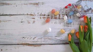 4k video. Beyaz ahşap masada lalelerle yuvarlanan çok renkli Paskalya yumurtaları. Geleneksel bahar kompozisyonu ilkbahar için Paskalya elementleri çiçekler ve yumurtalar. Bahar dekorasyonu konsepti