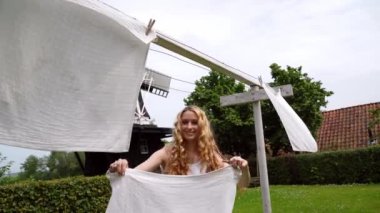 Geleneksel Hollanda elbisesi giymiş, tahta ayakkabılı, sarı takunyalı, dışarıda çamaşır ipine asılı bir kadın. Rüzgarlı bir günde Hollanda 'nın arka planında çamaşır kurutmak. retro vintage tarzı 