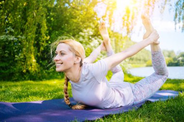Parkta yoga yapan genç bir kadın. Kız yoga pozisyonunda egzersiz yapıyor. Nilüfer pozisyonunda oturup yoga yapan mutlu ve sağlıklı bir kadın. Gün batımında meditasyon ve spor.
