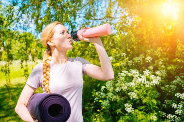Sporcu kadın yoga antrenmanına minderle gidiyor. Spor salonunda egzersiz yapmaya hazır. Sportif kız antrenmandan önce yoga minderi ve su şişesi tutuyor. Aktif spor yaşam tarzı ve sağlık kavramı.