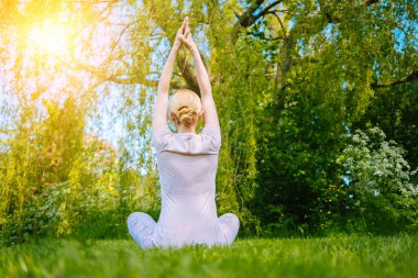 Parkta yoga yapan genç bir kadın. Kız yoga pozisyonunda egzersiz yapıyor. Nilüfer pozisyonunda oturup yoga yapan mutlu ve sağlıklı bir kadın. Gün batımında meditasyon ve spor.