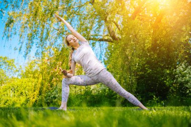 Parkta yoga yapan genç bir kadın. Kız yoga pozisyonunda egzersiz yapıyor. Nilüfer pozisyonunda oturup yoga yapan mutlu ve sağlıklı bir kadın. Gün batımında meditasyon ve spor.
