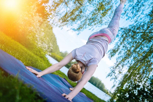 Mujer joven haciendo yoga asana en parque. chica estirando ejercicio en posición de yoga. mujer feliz y saludable sentada en posición de loto y practicando yoga. meditación y deporte al atardecer al aire libre. — Foto de Stock