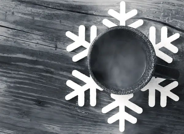 Tasse mit heißem Kaffee auf der Unterlage in Form einer Schneeflocke — Stockfoto