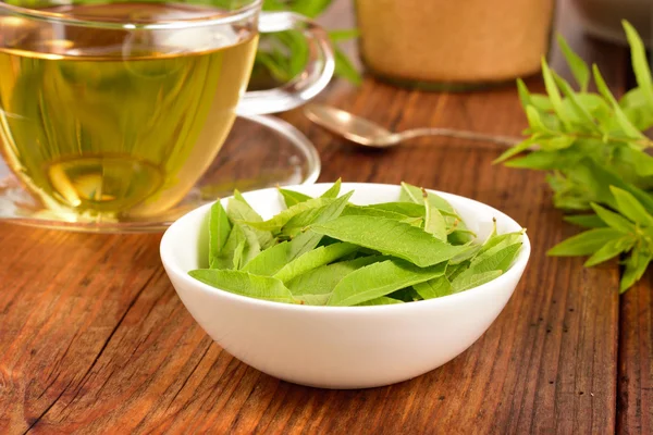 Zitronenverbene Blätter und Tee auf dem Tisch. — Stockfoto