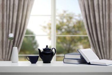 Bir yığın kitap ve beyaz bir masada bir pencerenin arka planına ve ağaçlı bir bahçeye karşı taze bir çay. Eğitim öğrenme konsepti.