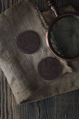 Numismatikler. Eski koleksiyon paraları ve ahşap bir masanın üzerinde büyüteç. Karanlık arka plan. Üst görünüm.
