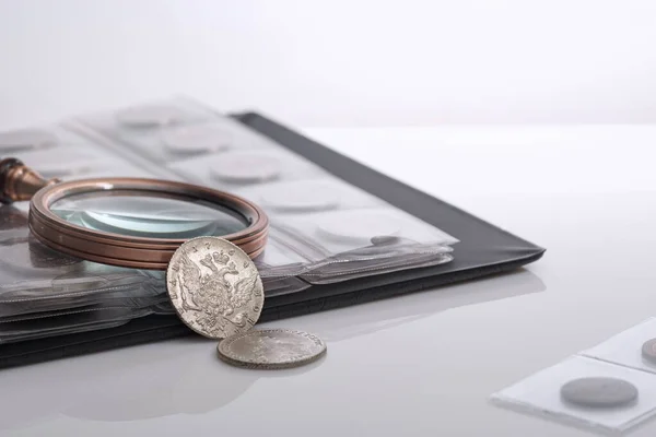Numismatikler. Eski koleksiyon paraları ve masanın üzerinde bir büyüteç. Hafif arkaplan.