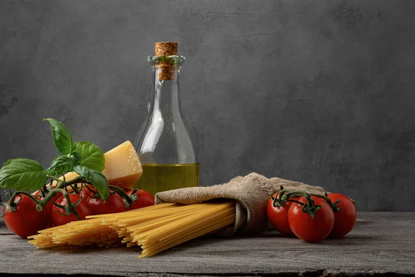 新鮮なトマトとスパゲティパスタ バジルのハーブ 古い木製のテーブルの上にハードパルメザンチーズとオリーブオイル 暗い背景 — ストック写真