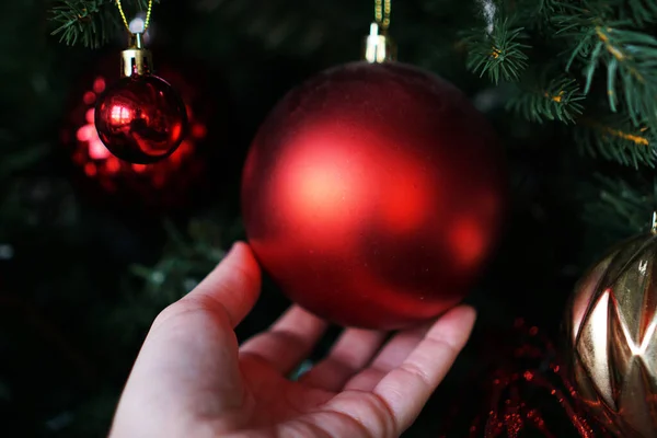 Weibliche Hand hält eine rote Weihnachtskugel auf dem Hintergrund eines Weihnachtsbaums — Stockfoto
