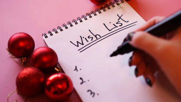 Mujer escribiendo su lista de deseos. Diseño festivo sobre fondo rosa con bolas rojas —  Fotos de Stock