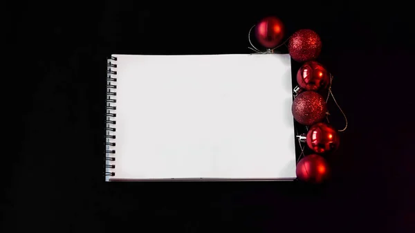 Open blank notebook, Christmas balls on black background — Stock Photo, Image