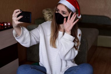 Yeni yıl video çağrıları konsepti. Noel Baba şapkalı bir kızın elinde cep telefonu var.