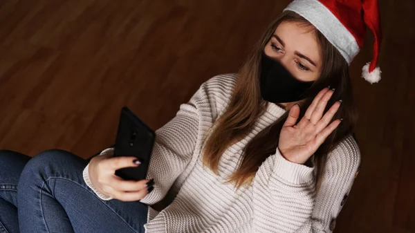 Año nuevo concepto de videollamadas. Una chica en Santa sombrero sostiene un teléfono móvil —  Fotos de Stock