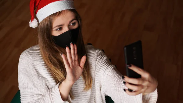 Año nuevo concepto de videollamadas. Una chica en Santa sombrero sostiene un teléfono móvil —  Fotos de Stock