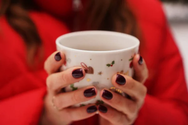 Manos femeninas sosteniendo la taza con bebida oscura caliente afuera en el día de invierno — Foto de Stock