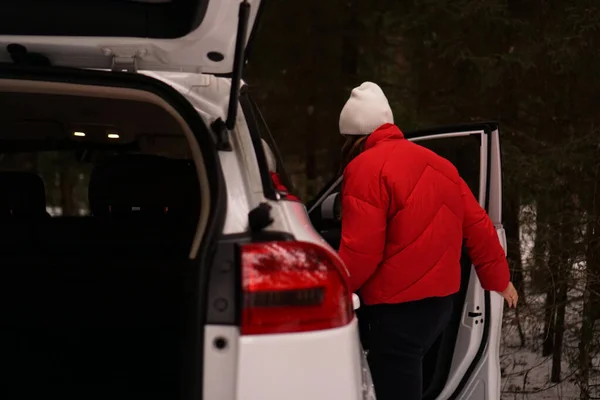 Fehér autó a téli erdőben. A vörös ruhás nő kinyitja az ajtót. — Stock Fotó