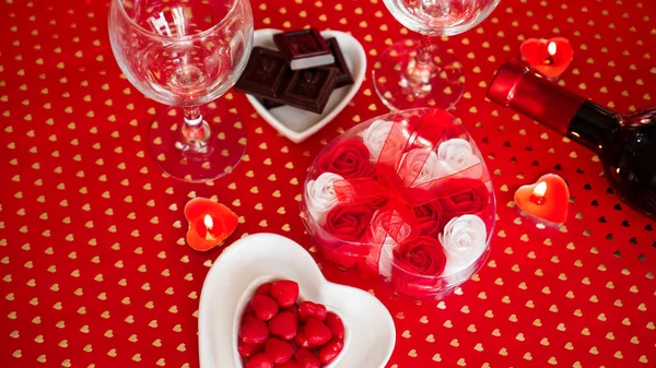 Valentines day. Bottle of vine, glasses, red roses, candles - red background