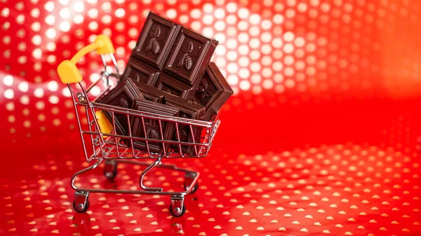 Čokoláda v nákupním vozíku na červeném pozadí. 14 únor prodej — Stock fotografie
