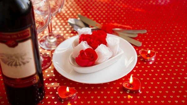 Valentines day. Bottle of vine, glasses, red roses, candles - red background