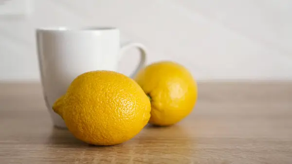 Два лимона на кухонном столе рядом с белой чашкой чая — стоковое фото
