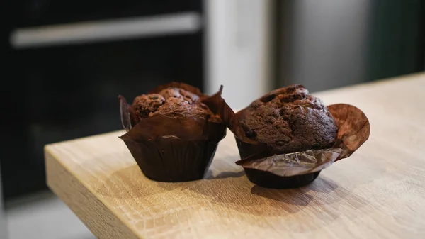 Dos magdalenas de chocolate en una mesa de madera contra la cocina moderna —  Fotos de Stock