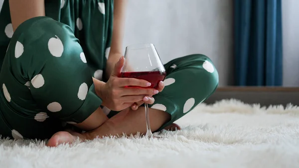 Девушка в зеленой пижаме в постели с бокалом красного вина — стоковое фото