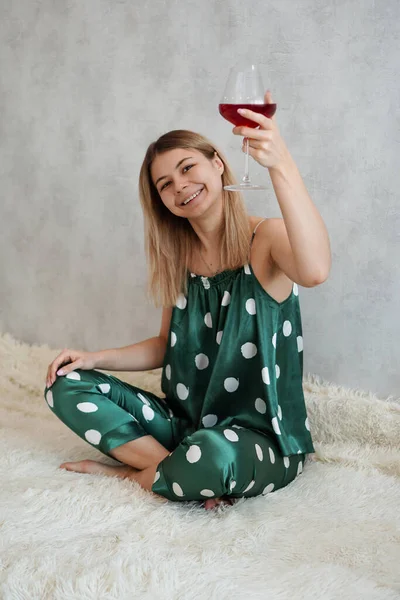 Девушка в зеленой пижаме в постели с бокалом красного вина — стоковое фото