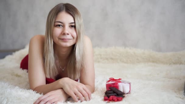Красивая блондинка лежит на диване рядом с подарком на День Святого Валентина — стоковое видео