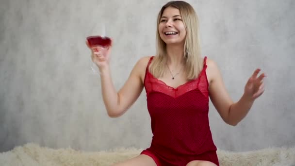 Beautiful blonde woman in bed drinks wine and dances. — Stock Video