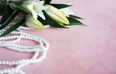 Beyaz zambaklar ve pembe bir arka planda inci kolye..