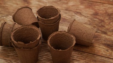 Ahşap bir arka planda fidanlar için boş turba kapları. Bahçıvanlık. Baharda bitki ve çiçek dikmek için bahçe aletleri hazırlama kavramı.