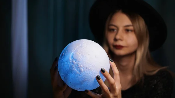 A young woman fortune teller in a hat is holding a magic ball.