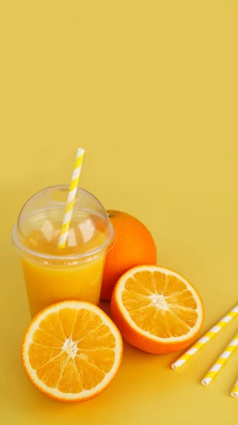Orange juice in fast food closed cup with tube on yellow background