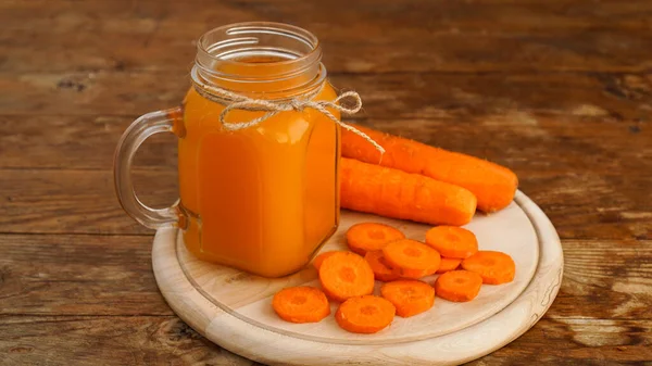 Bright orange carrot juice in a glass jar on a wooden background