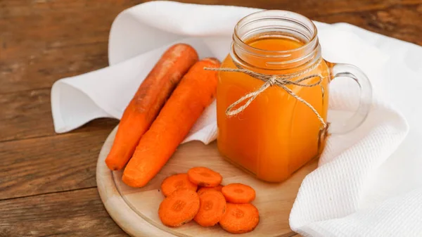 Bright orange carrot juice in a glass jar on a wooden background