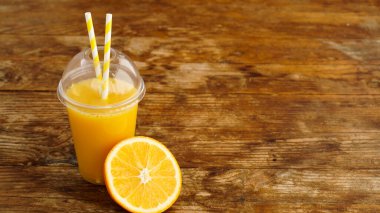Fast food bardağında portakal suyu ve ahşap masada tüpler. Taze yaz içkisi. Afiş için fotoğraf veya kafe ve menü reklamı