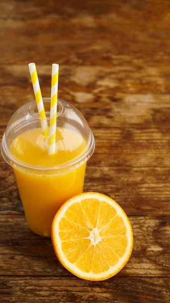 Orange juice in fast food closed cup with tubes on wooden table. Fresh summer drink. Photo for banner or advertisement of cafe and menu