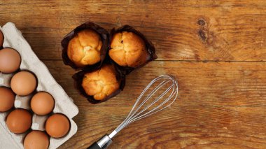 Kırsal ahşap arka planda pişmiş kek ve kek. Tepside yumurtalar, hamur çırpışı ve lezzetli taze kekler.