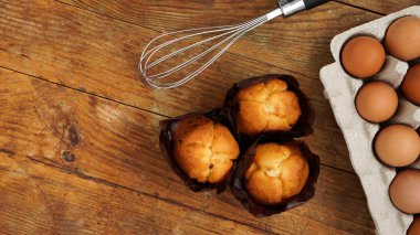 Kırsal ahşap arka planda pişmiş kek ve kek. Tepside yumurtalar, hamur çırpışı ve lezzetli taze kekler.