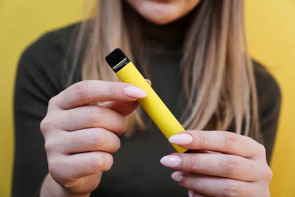 Amarelo cigarro eletrônico descartável na mão feminina. Fundo amarelo brilhante — Fotografia de Stock