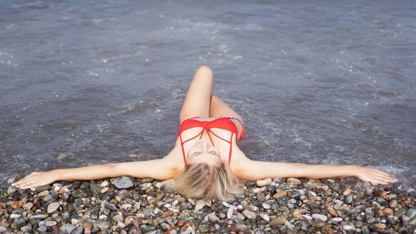 Красивая блондинка в красном купальнике загорает на брусчатом пляже у моря — стоковое фото