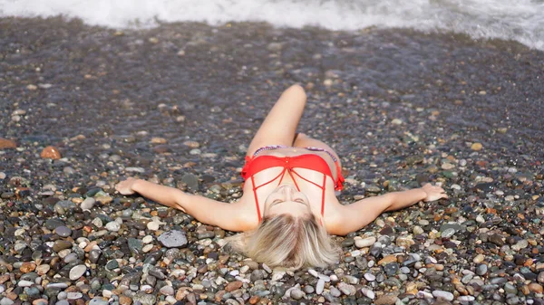 Красивая блондинка в красном купальнике загорает на брусчатом пляже у моря — стоковое фото