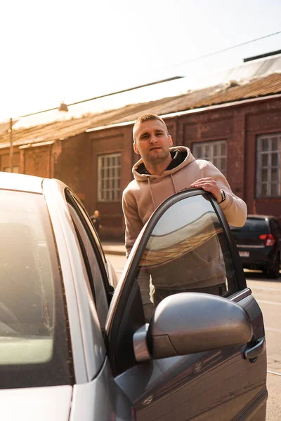 Молодой человек рядом со своей машиной в солнечный день на улице старого города. — стоковое фото