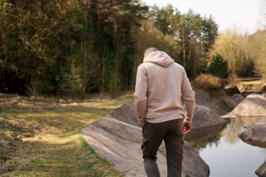 Bir adam ormanın içinde kürek çeken bir kanalın ya da dağ nehrinin yanında yürüyor.